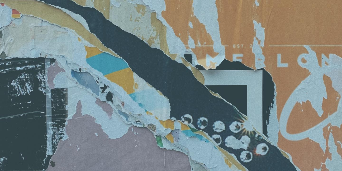 Torn fly posters layered under graffiti on a wall.