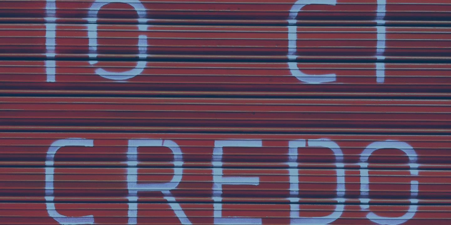 A red shutter door bears a large painted message reading 'io ci credo'