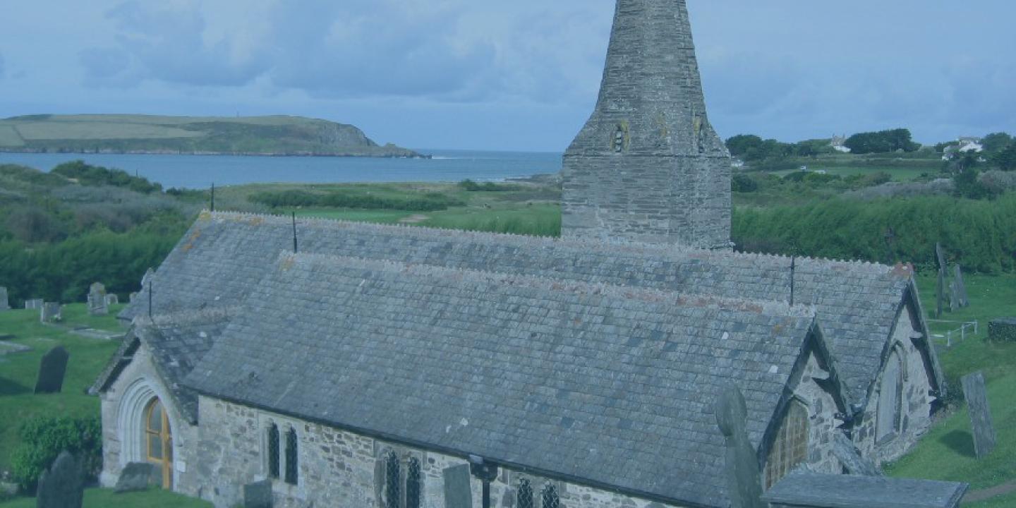 A stone church and tower emerge from the hillside with the sea in the distance.