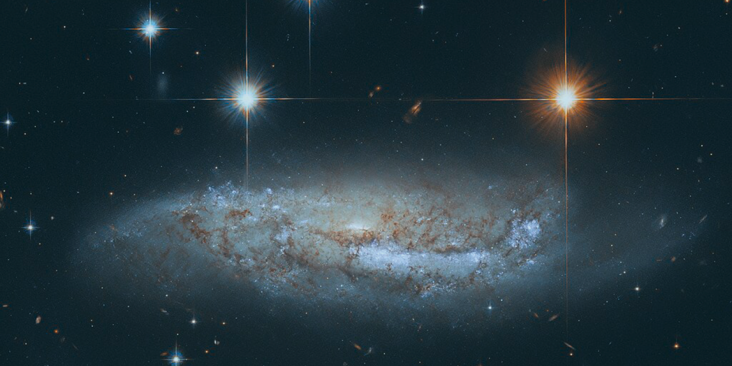 Four stars scintilate above a spiral galaxy viewed from the side.