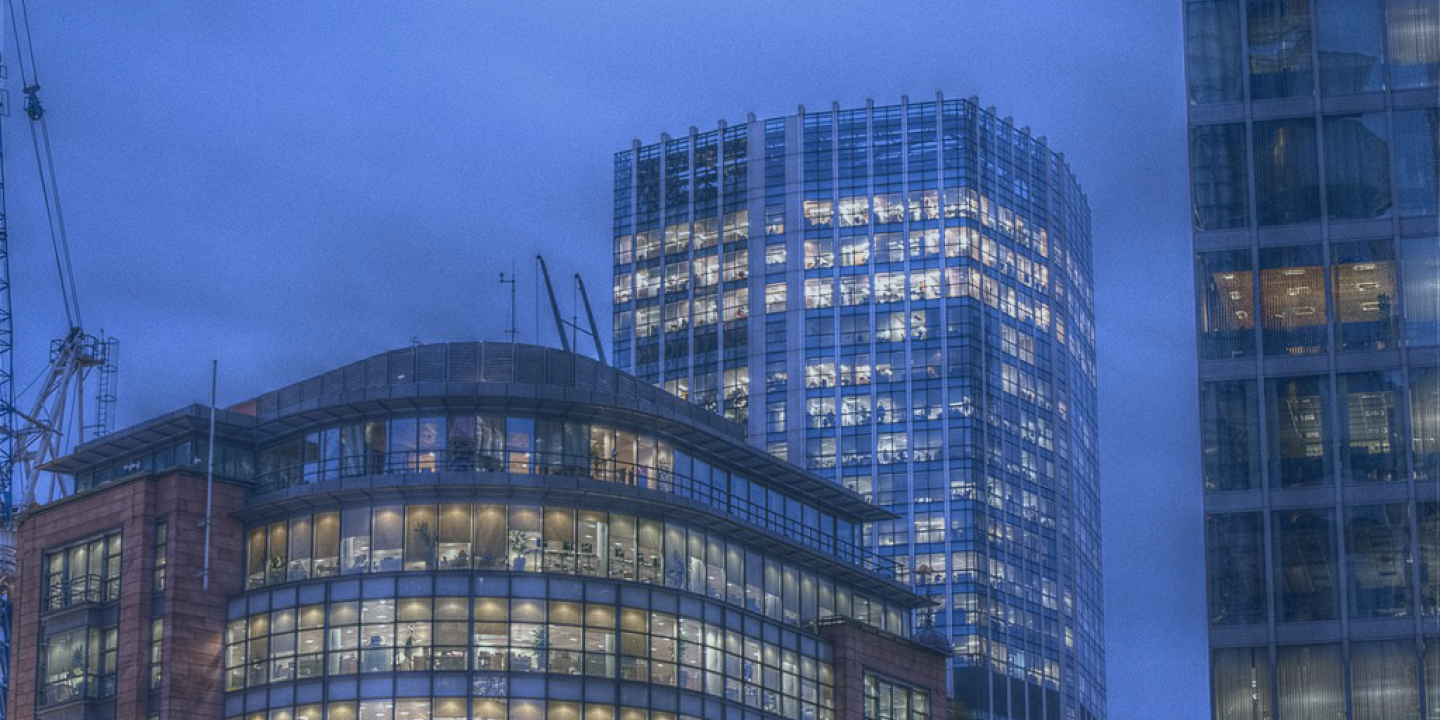 At twlight, the lit office windows of two tower blocks contrast with a darkening sky