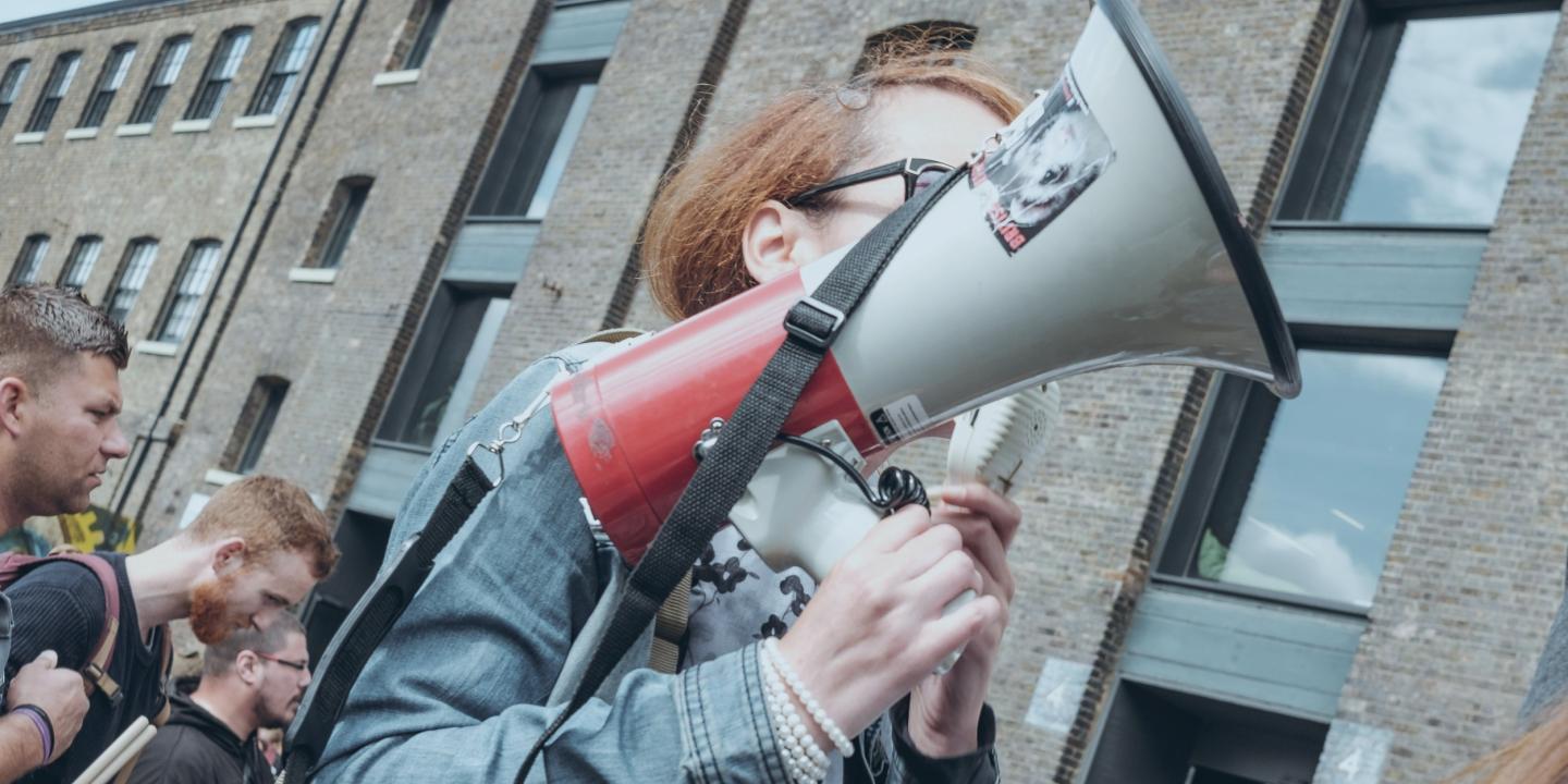 A protestor hold a megaphone up at a demonstration outside a building