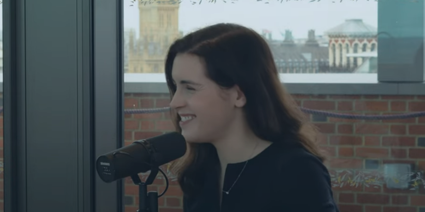 A woman smiles as she speaks into a microphone. In the background is Big Ben.