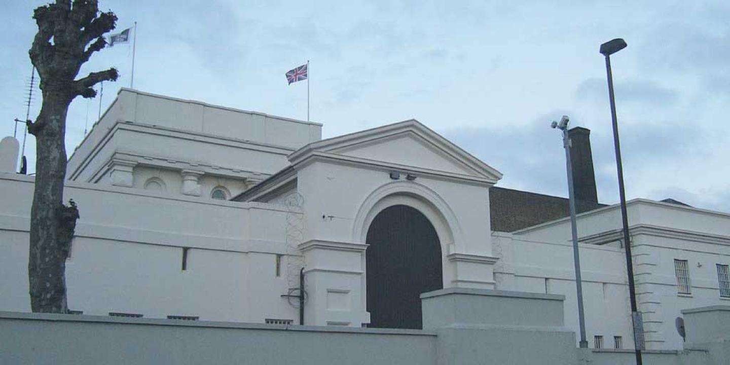 An arched gateway to a prison sits behind a low raised wall. No windows are visible
