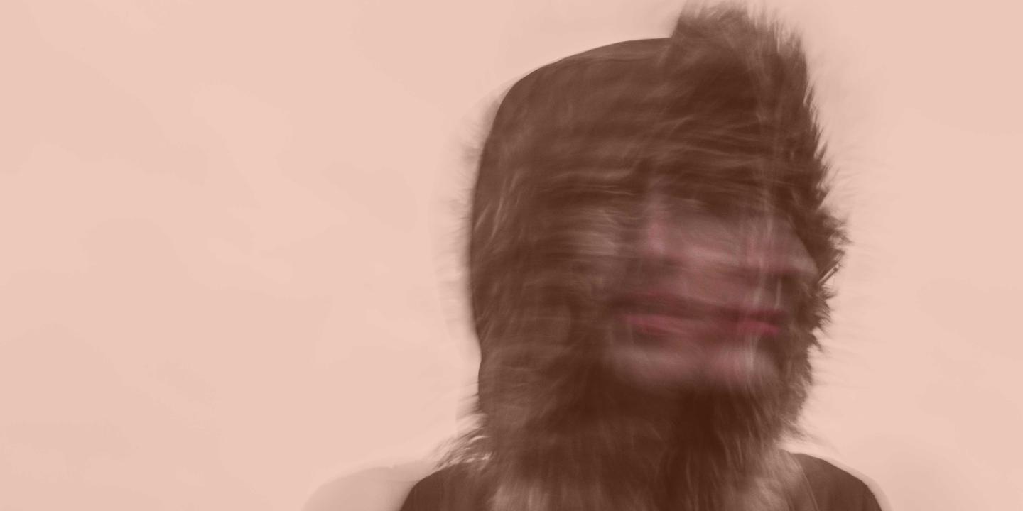 A blurred exposure of a person under a hood turning their head to the side.