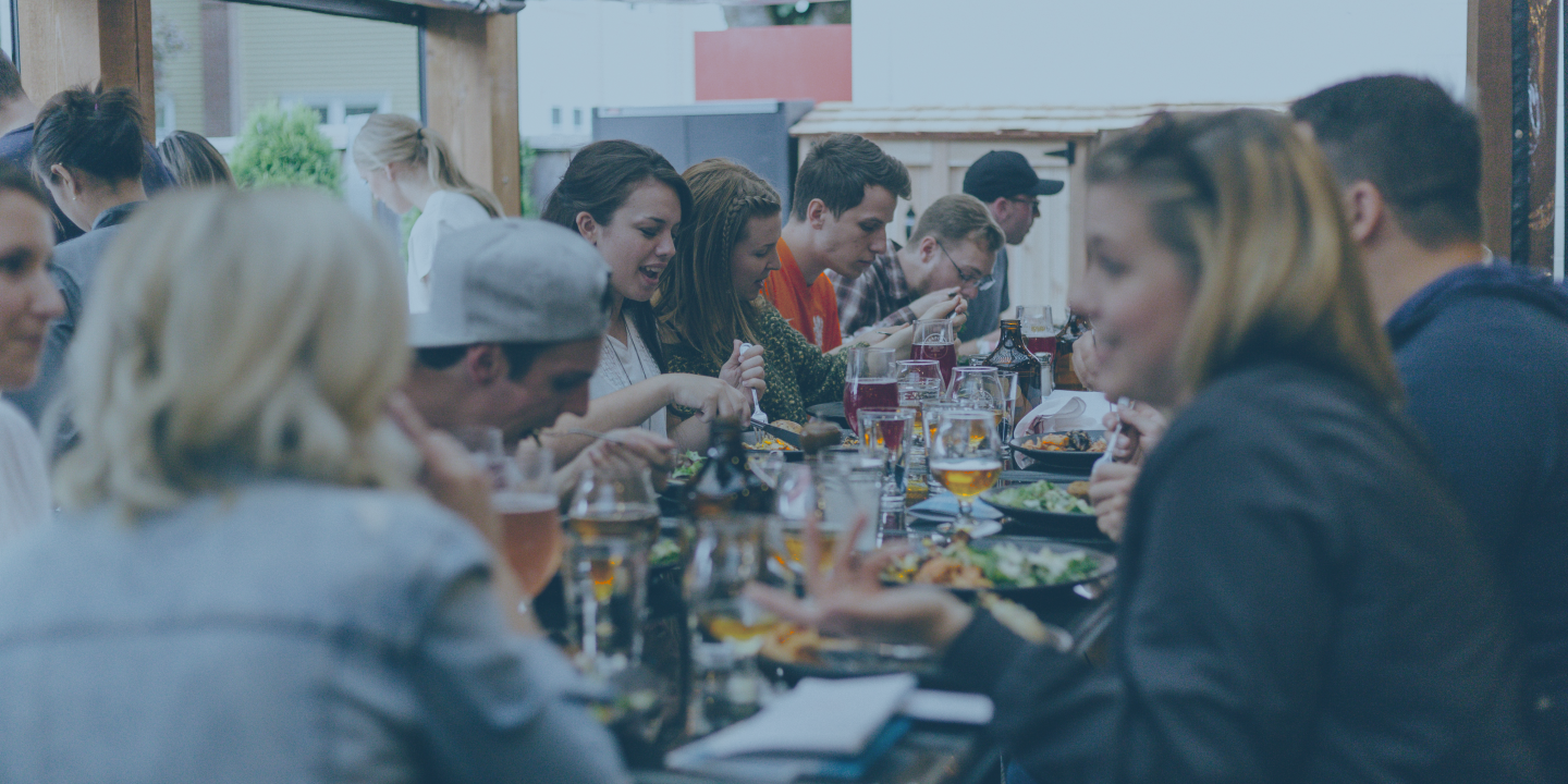 A large group of friends sit at a crowded table and share a meal together.