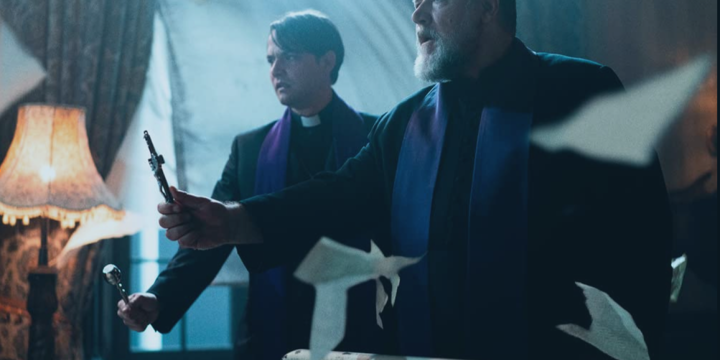 A priest holds a cross up in his hand in a chaotic environment while a colleague looks on