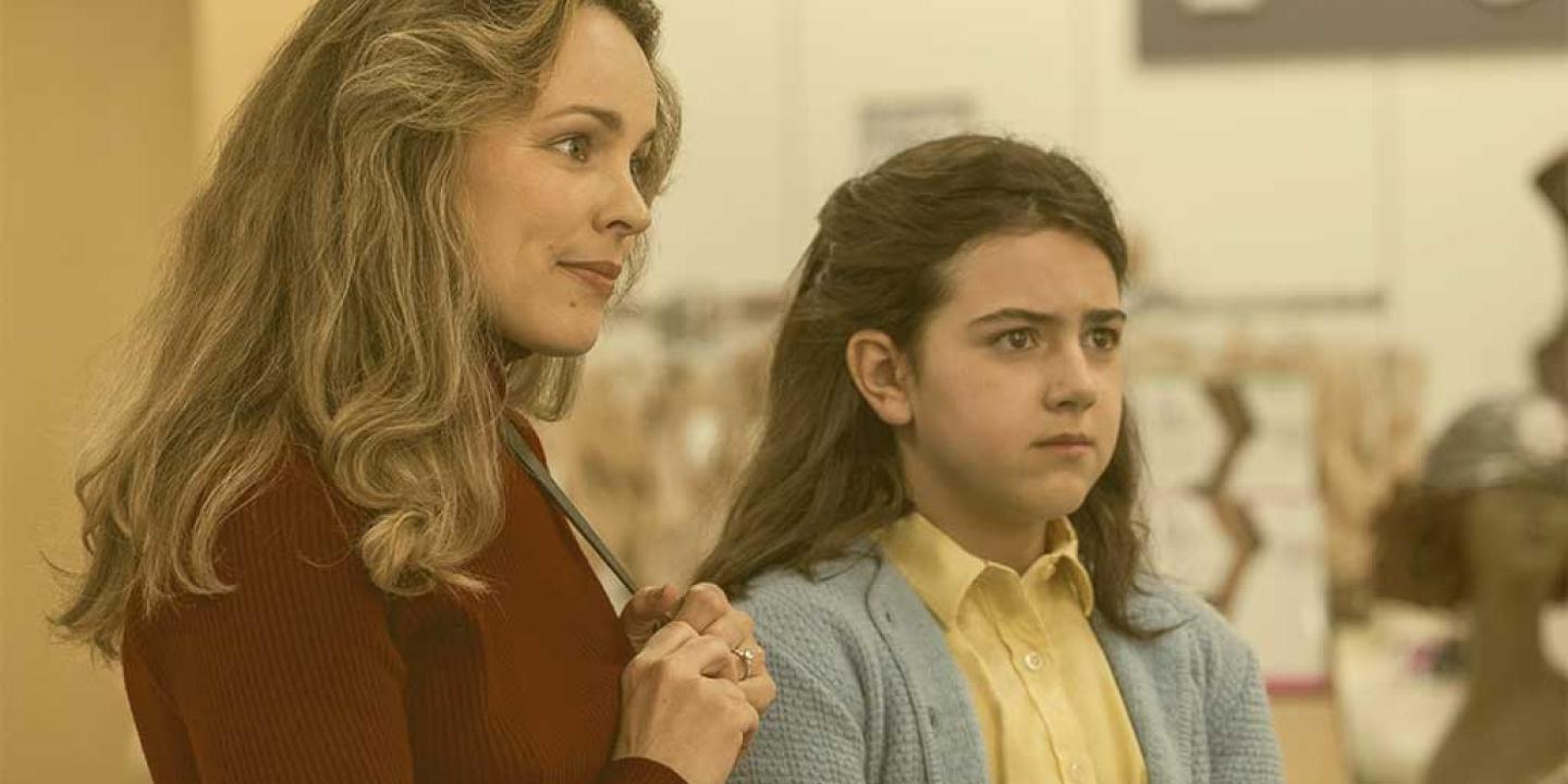 A mother and child, wearing 70s clothing, look to the left.
