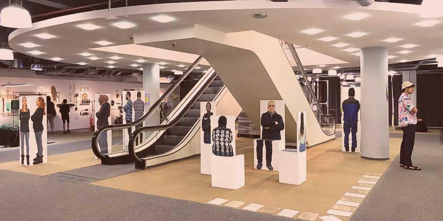 Between and around two escalators in a library, stand paintings of different people.