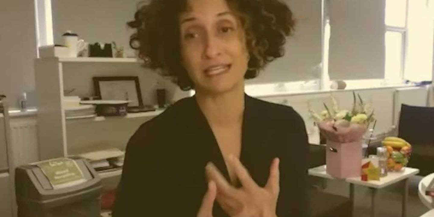 A head teacher sits at her desk, holding her hands in a gesture in front of her.