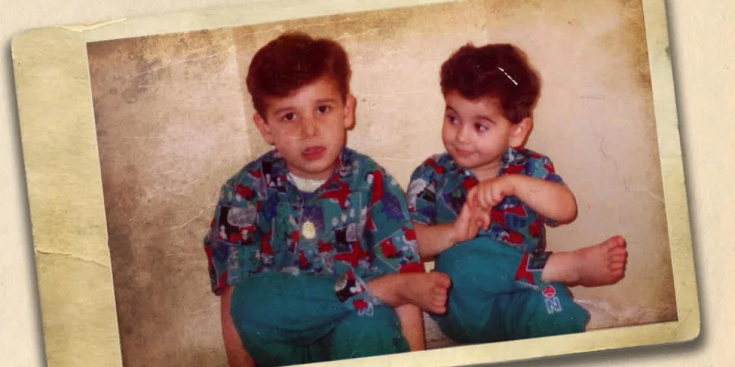 Two young brothers sit next to other, the younger looks to the elder.