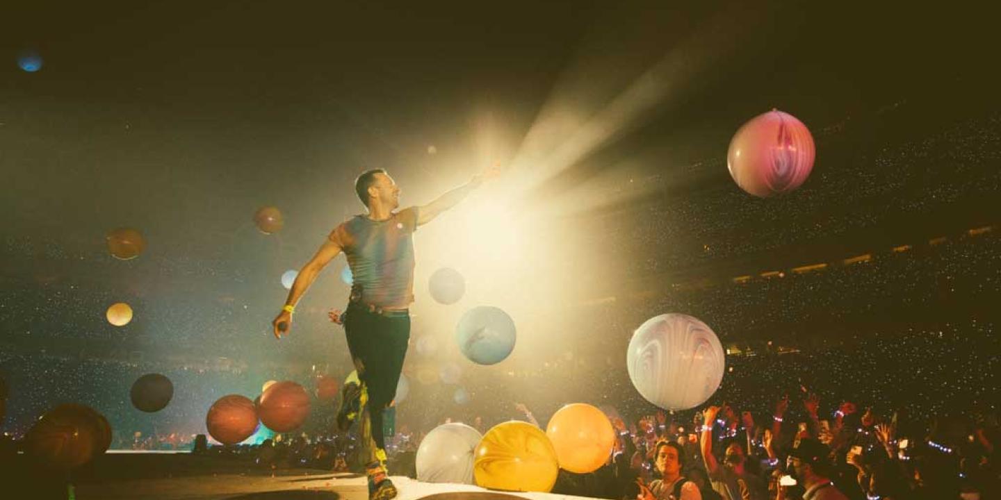 A singer struts a stage pointing to the spotlight as coloured orbs float down.