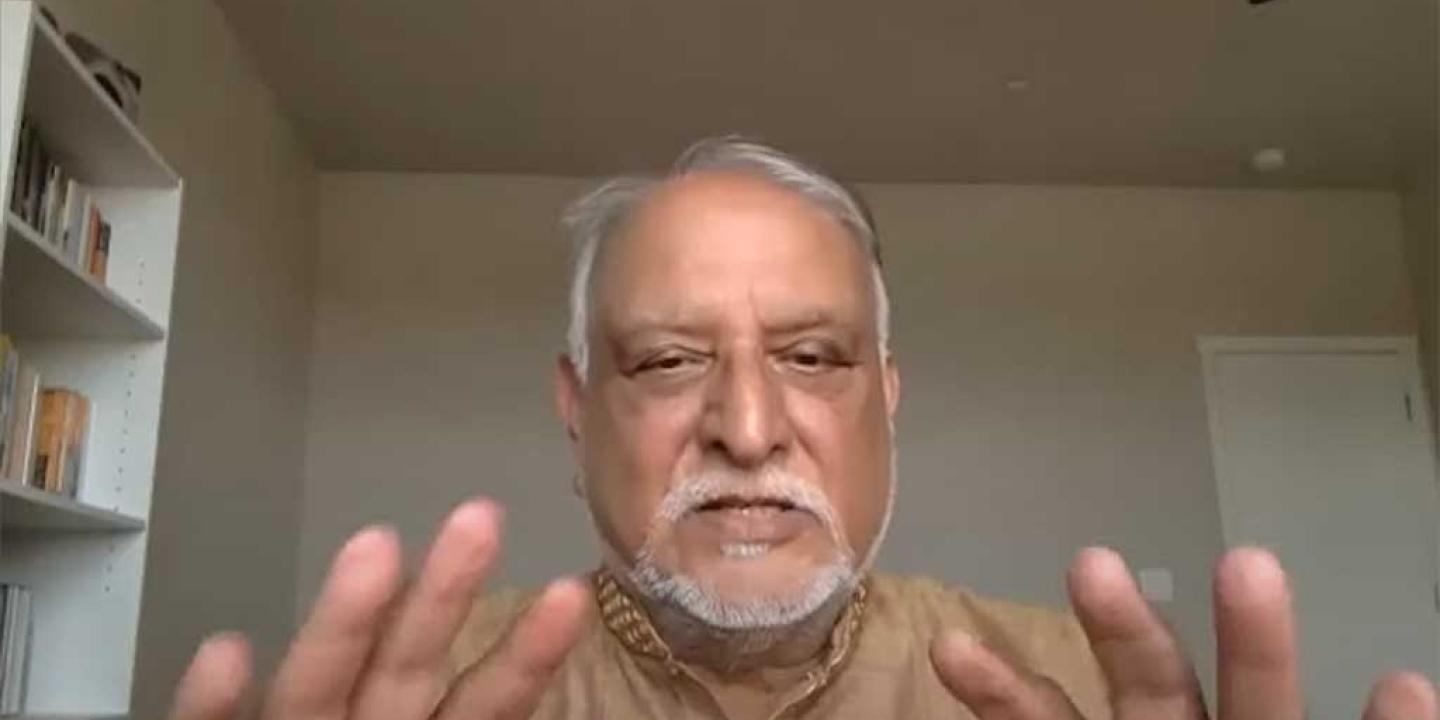 A man holds both hands up as he talks to a web cam