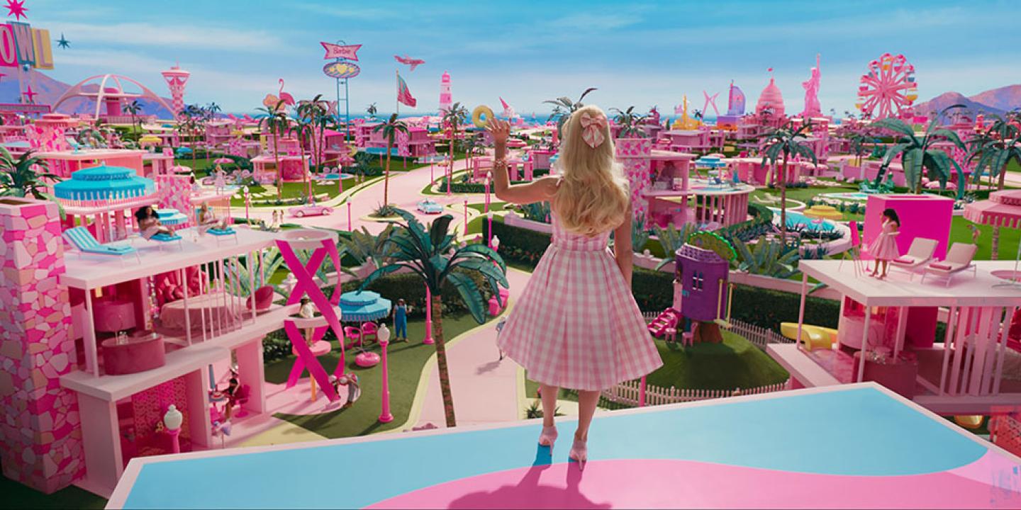 Barbie stands on a balcony and waves while looking out over her city.