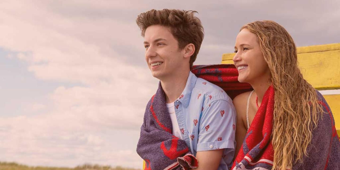 A young couple sit next to each other on a beach sharing a towel.
