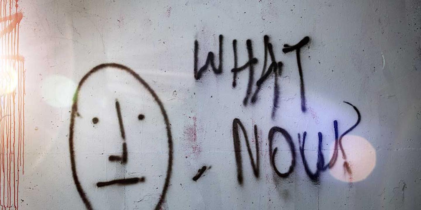 A graffited wall shows a stick man face next to 'what now'