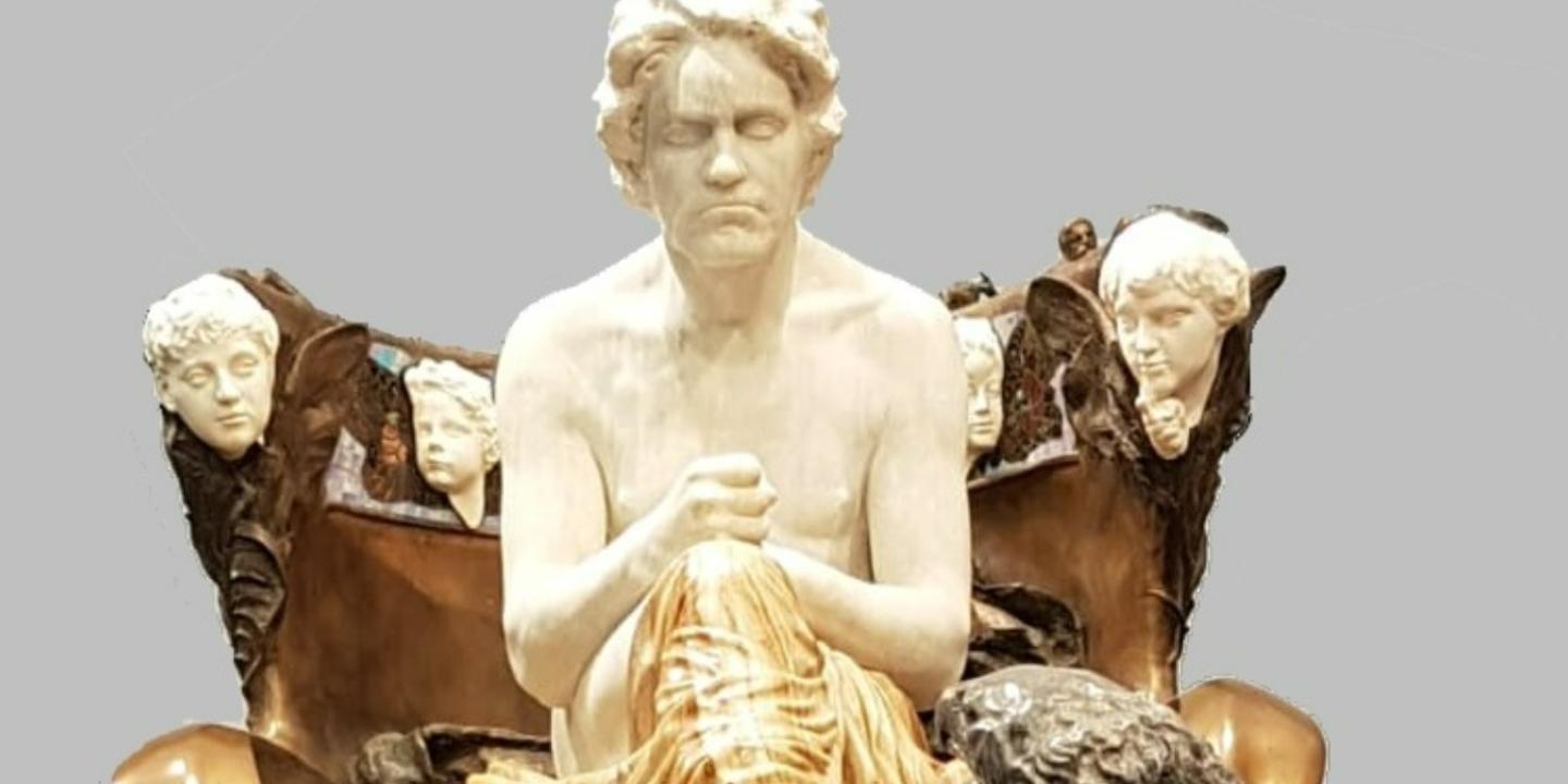 Agrand statue of Beethoven as a classical hero seats him on a throne on a dias.