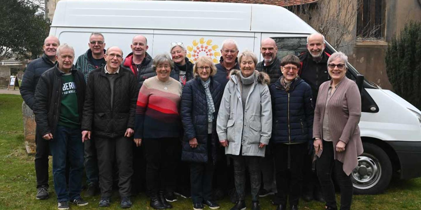 A group of people stand in front of the side of a van marked 'Furniture Friends.