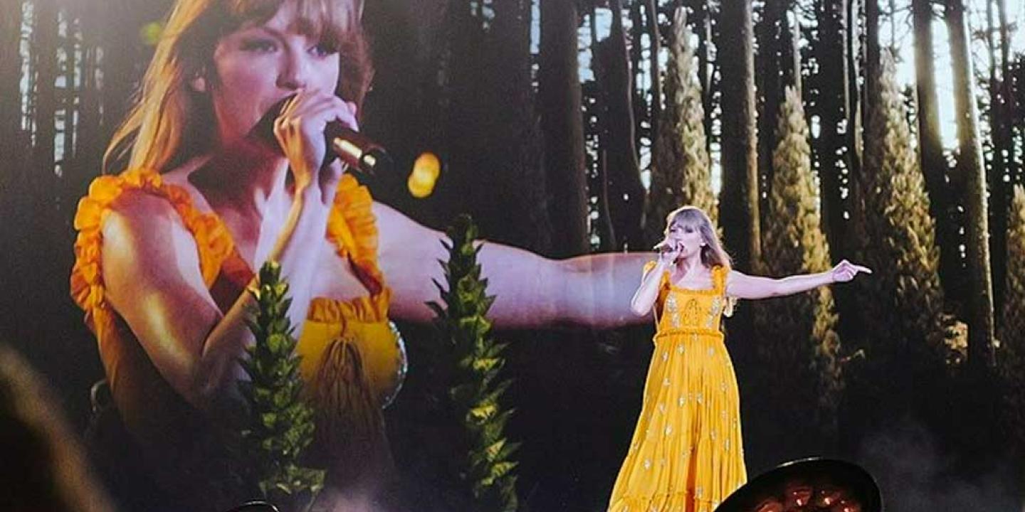 Taylor Swift wears a long yellow dress and signs with an outstretched arm against a backdrop of woods and a close up her singing beside it.