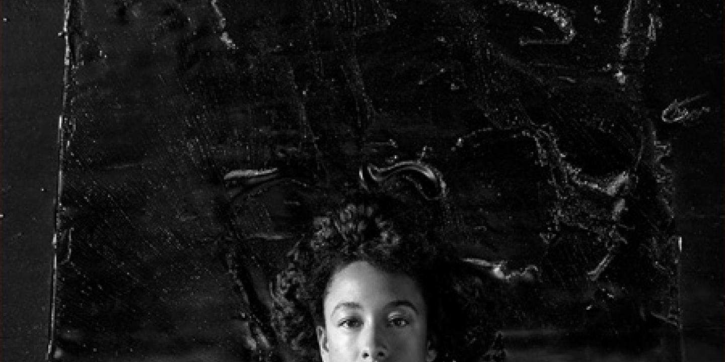 A black and white portrait of a young woman's head against a dark textured background.
