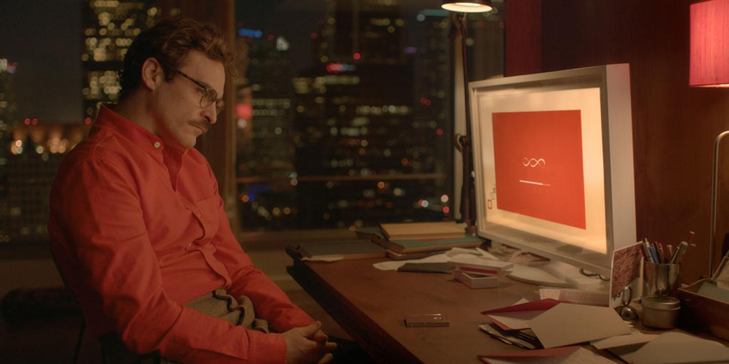 A man in a red shirt slumps in his seat while a computer screen shows a dialogue screen