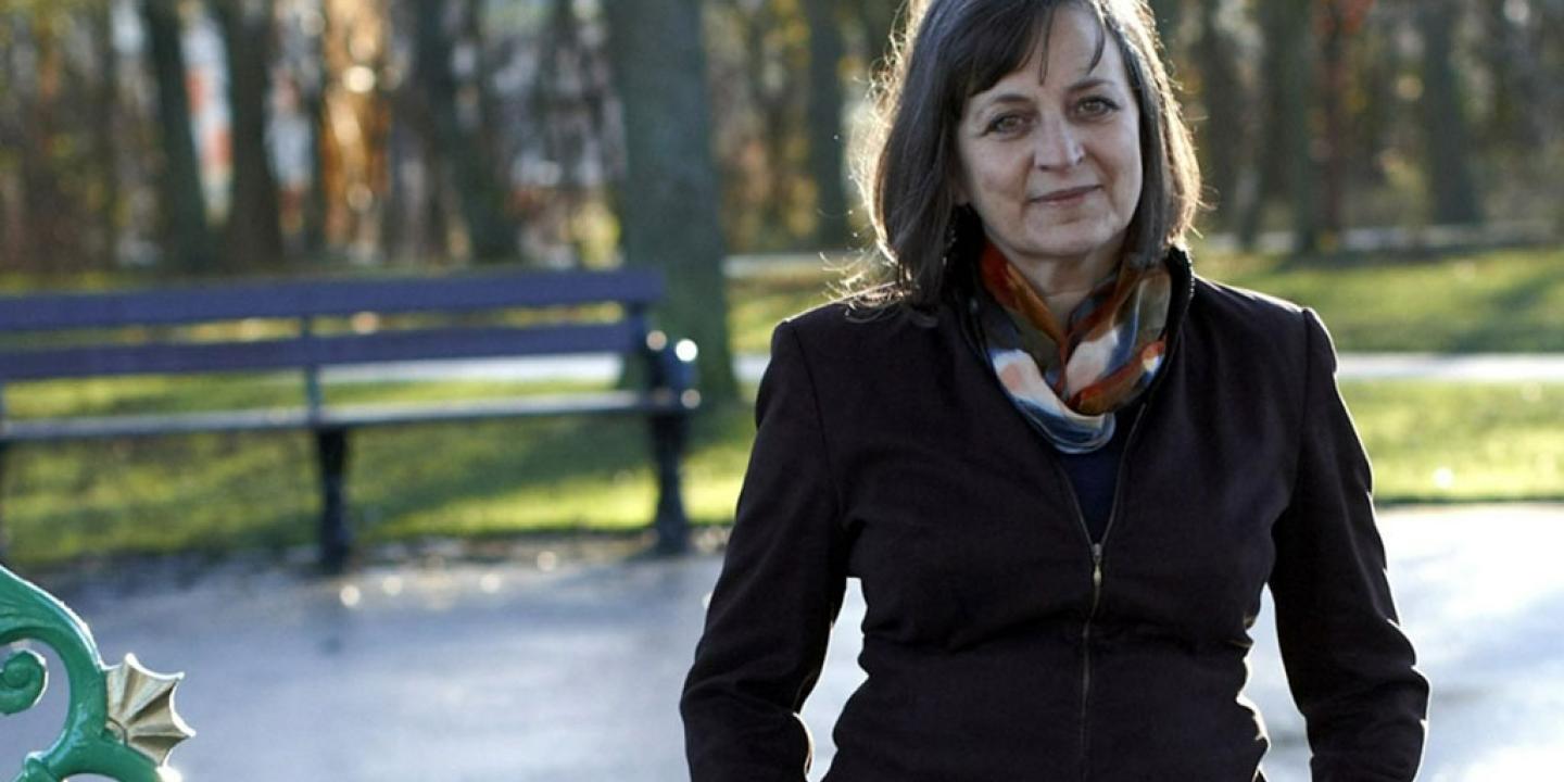 A woman stands in an autumnal-looking park, with her hands in her pockets