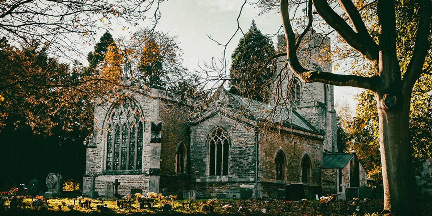 An autumnal scene of a church yard and church framed by leafless trees.