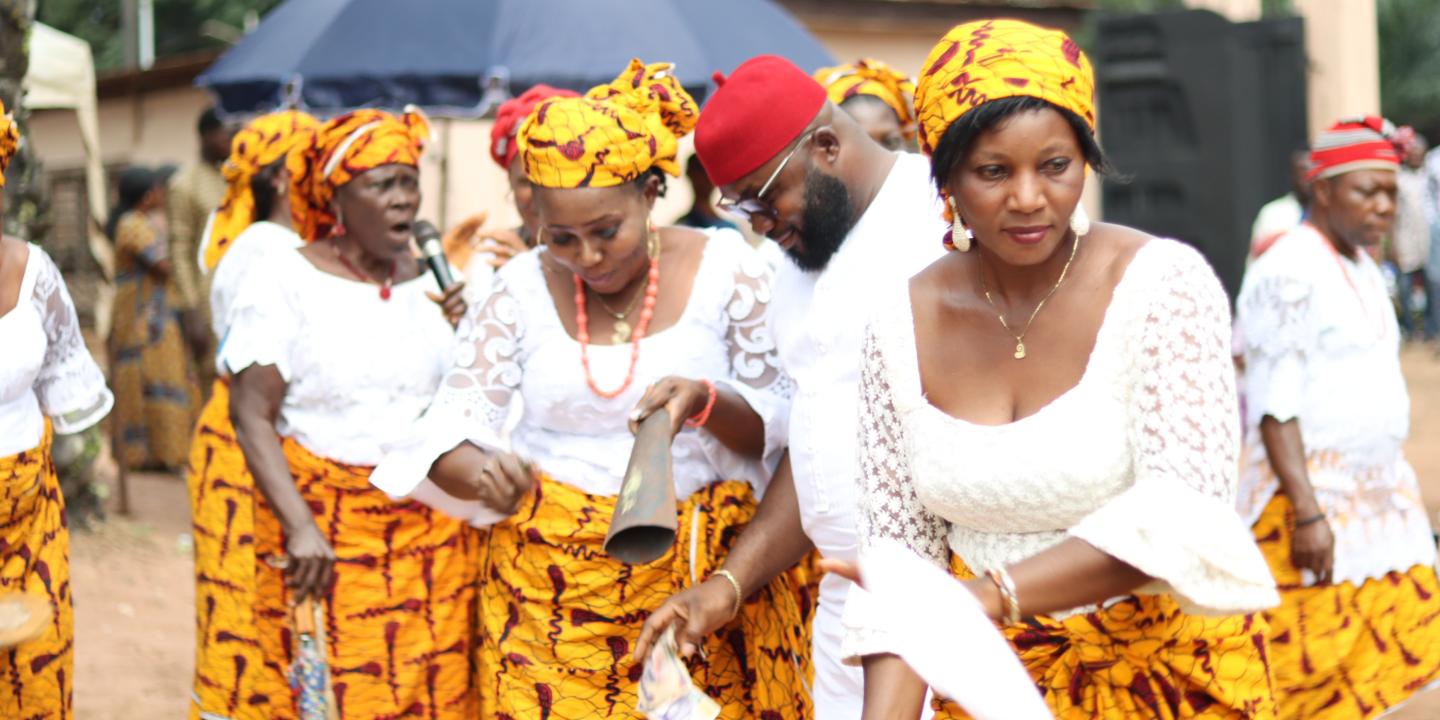 A group of women stand and dance at a celebration in the street, wearing matching skirts..