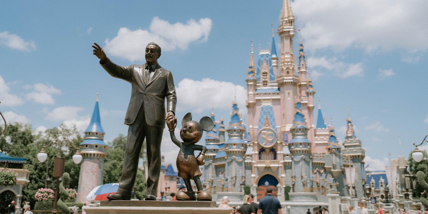 A statue of Walt Disney holding hands with Mickey Mouse in front of Cinderella's Castle
