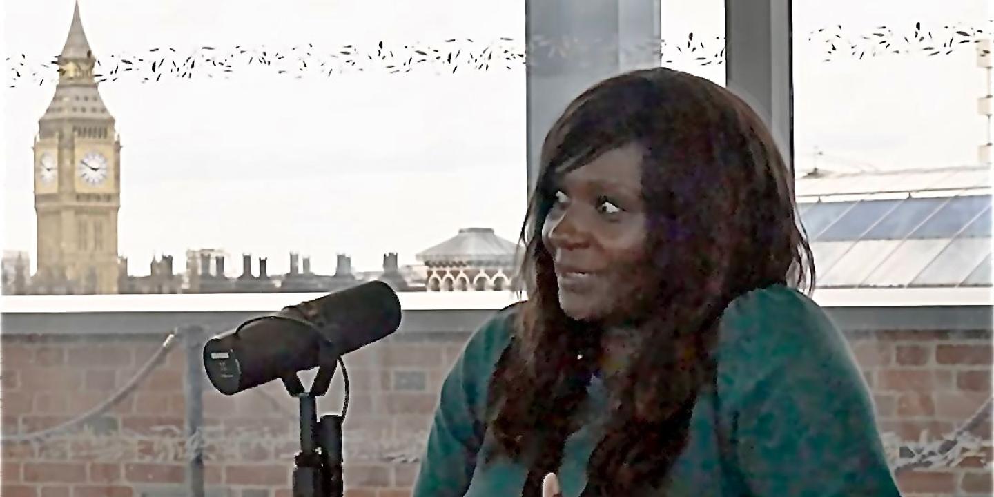 A women sits in beside a microphone taking.