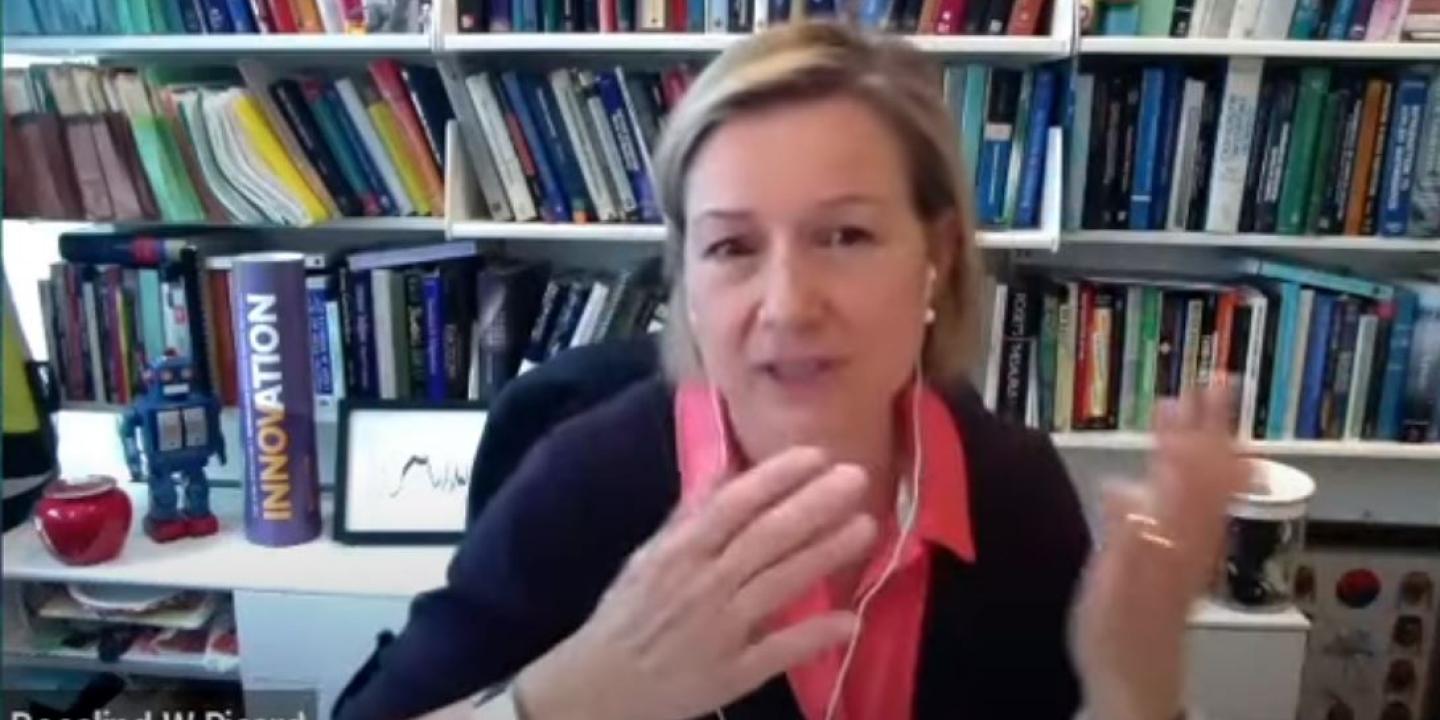 a woman at a desk video call gestures with her hands to make a point.
