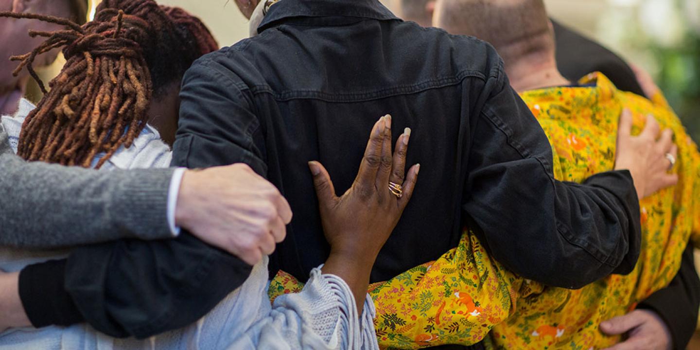 A group of grieving friends with their hands on each others backs.