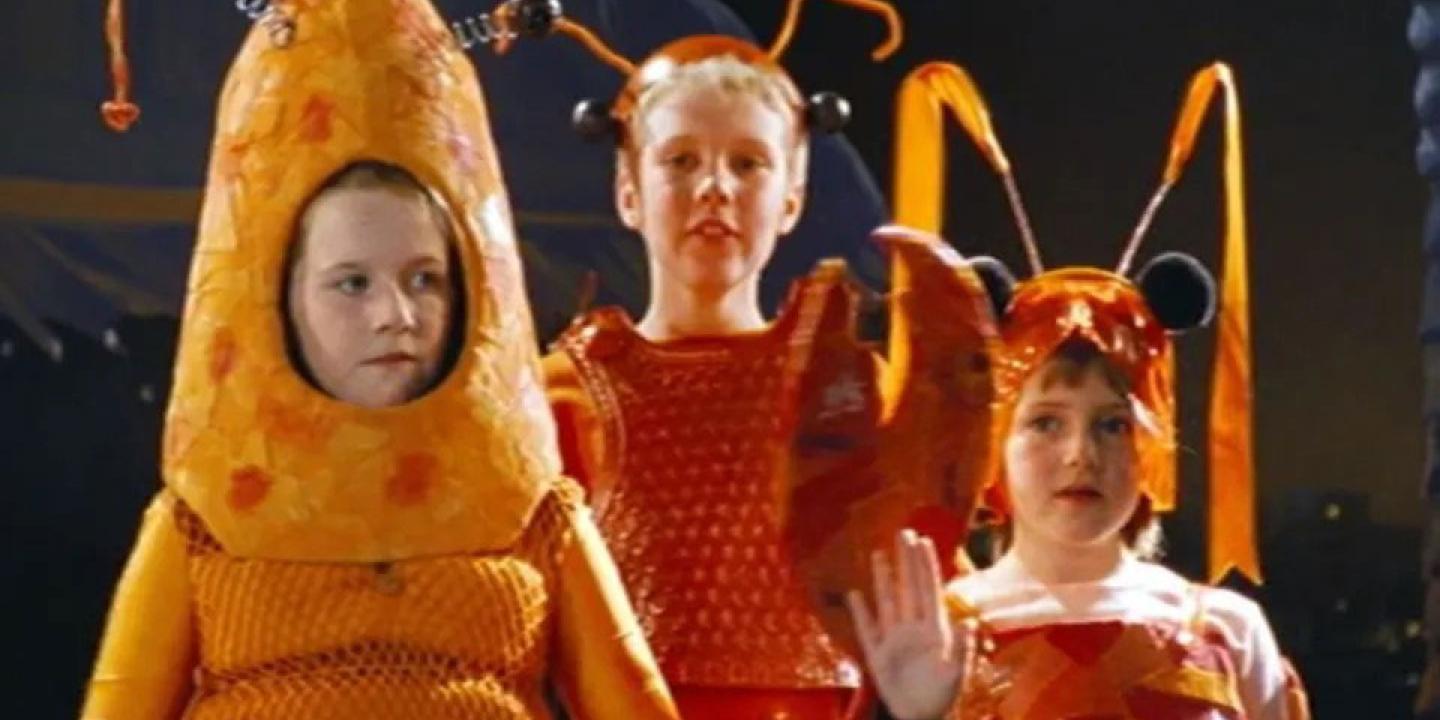 Three children dressed as orange lobsters stand sheepishly on a stage.