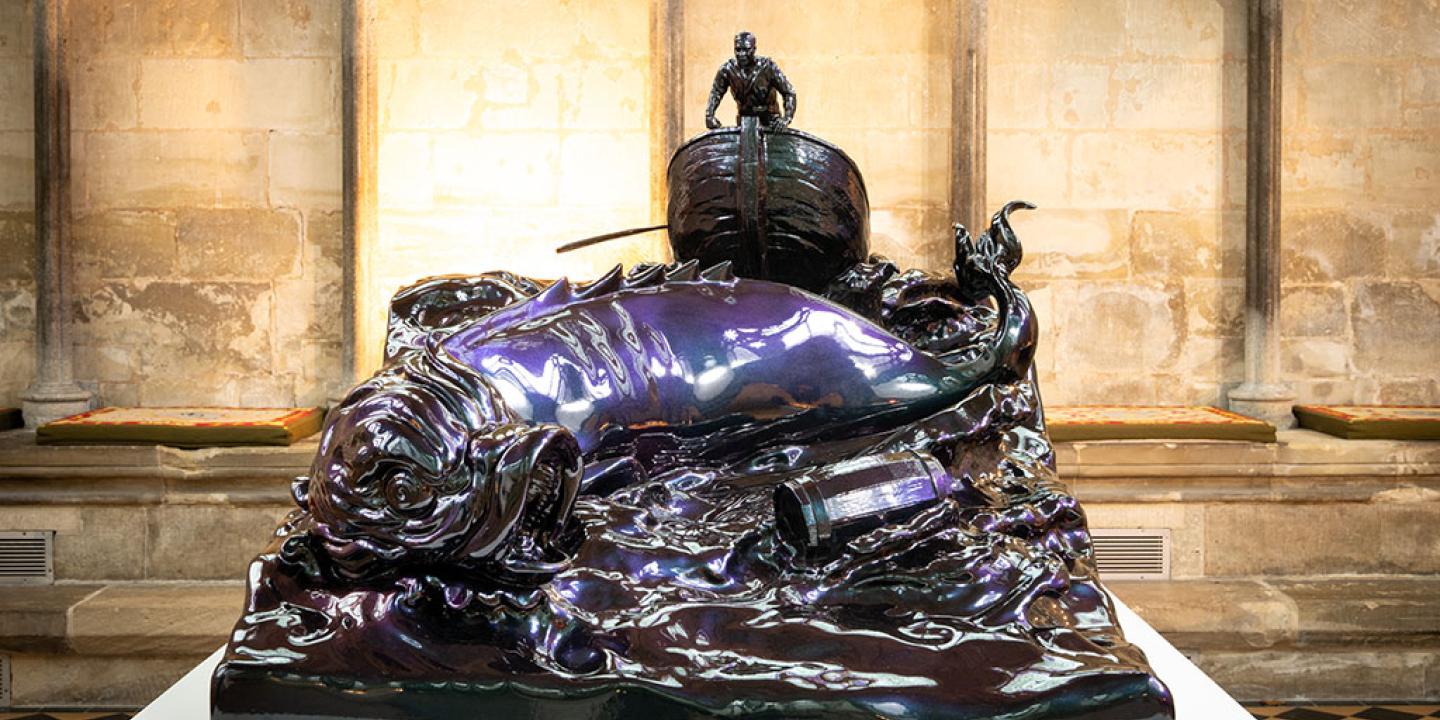 A bronze sculpture of a small boat and sea monster tossed in the waves.