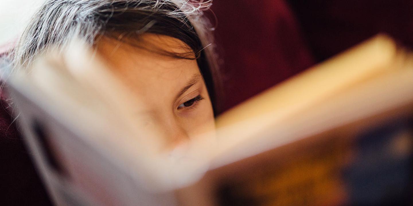 A close up of face, showing an eye, mostly obscured by a closely-held open book.