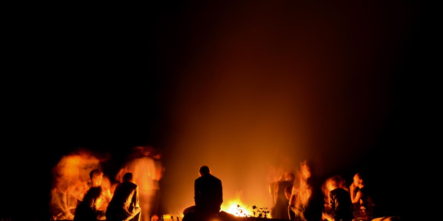 People sitting around a campfire are silhouetted against the night.