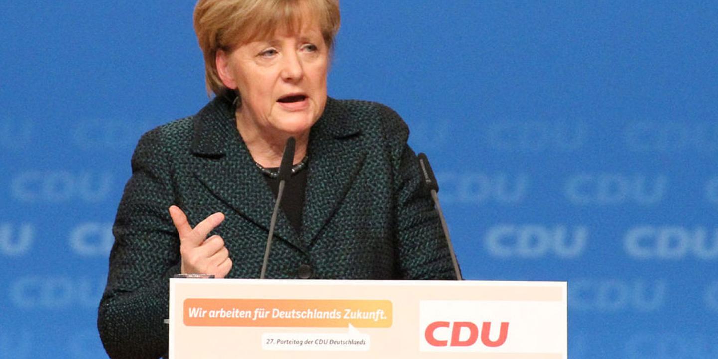 A politician stands a labelled lectern speaking and gesticulating with a hand.