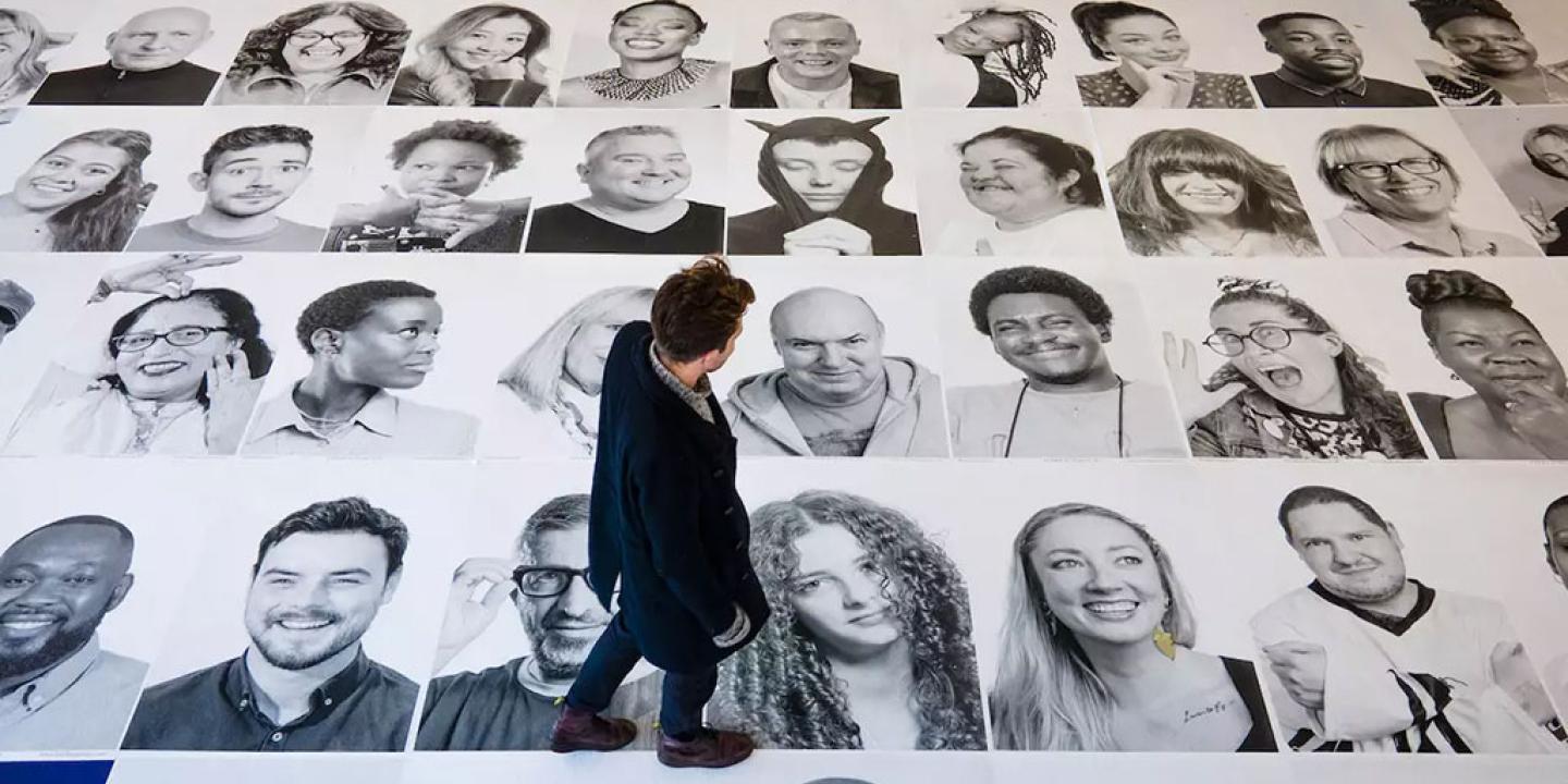 Looking down on a man walking across a grid of large black and white portrait photographs of people's faces