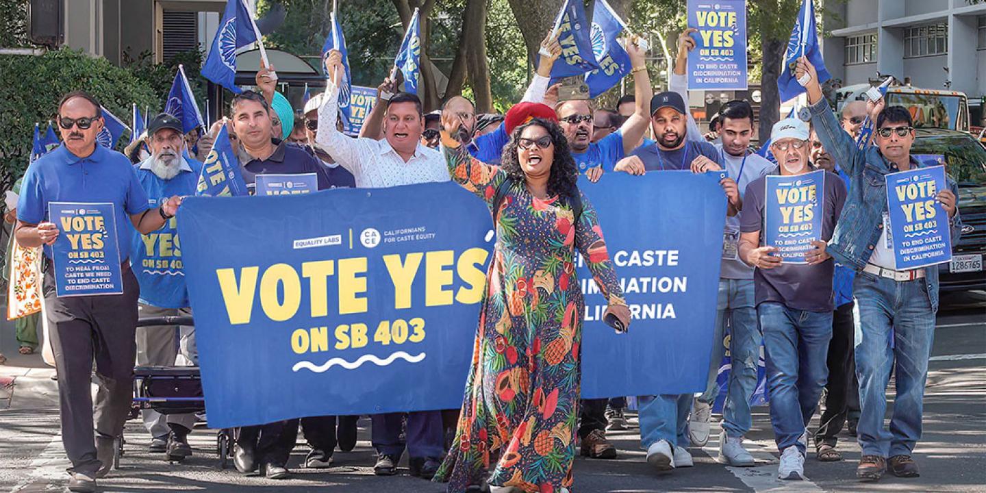 A group of protesters march behind a banner waving flags.