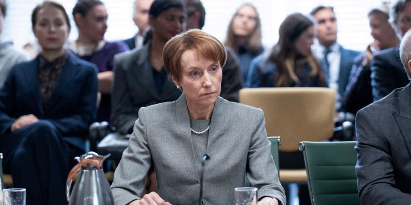 A tense-looking woman, sitting at  desk, stares into the middle disance.