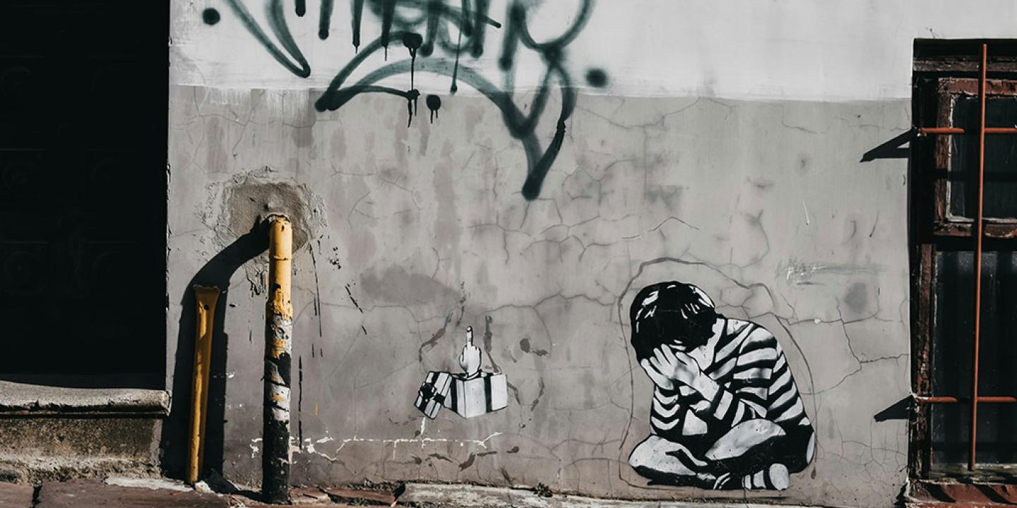 A grey and white wall graffited with a tag a image of a person crumpled and crying.