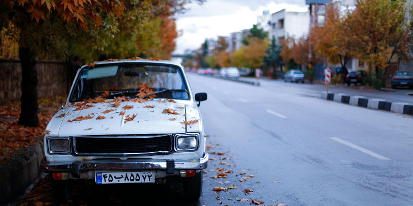 A somewat beaten white car parked on the side of a street.