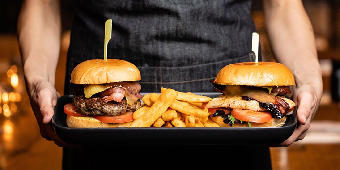 Two stuffed cheeseburgers are carried on a tray.
