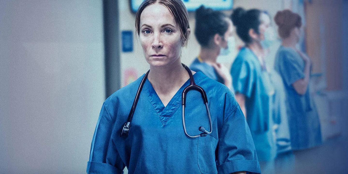A doctor in blue scrubs stands looking exhausted.