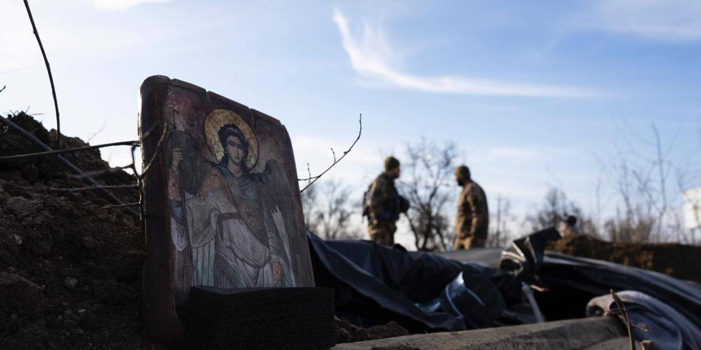 A religious icon is propped on the side of a trench, a soldier can be seen further down the trench.