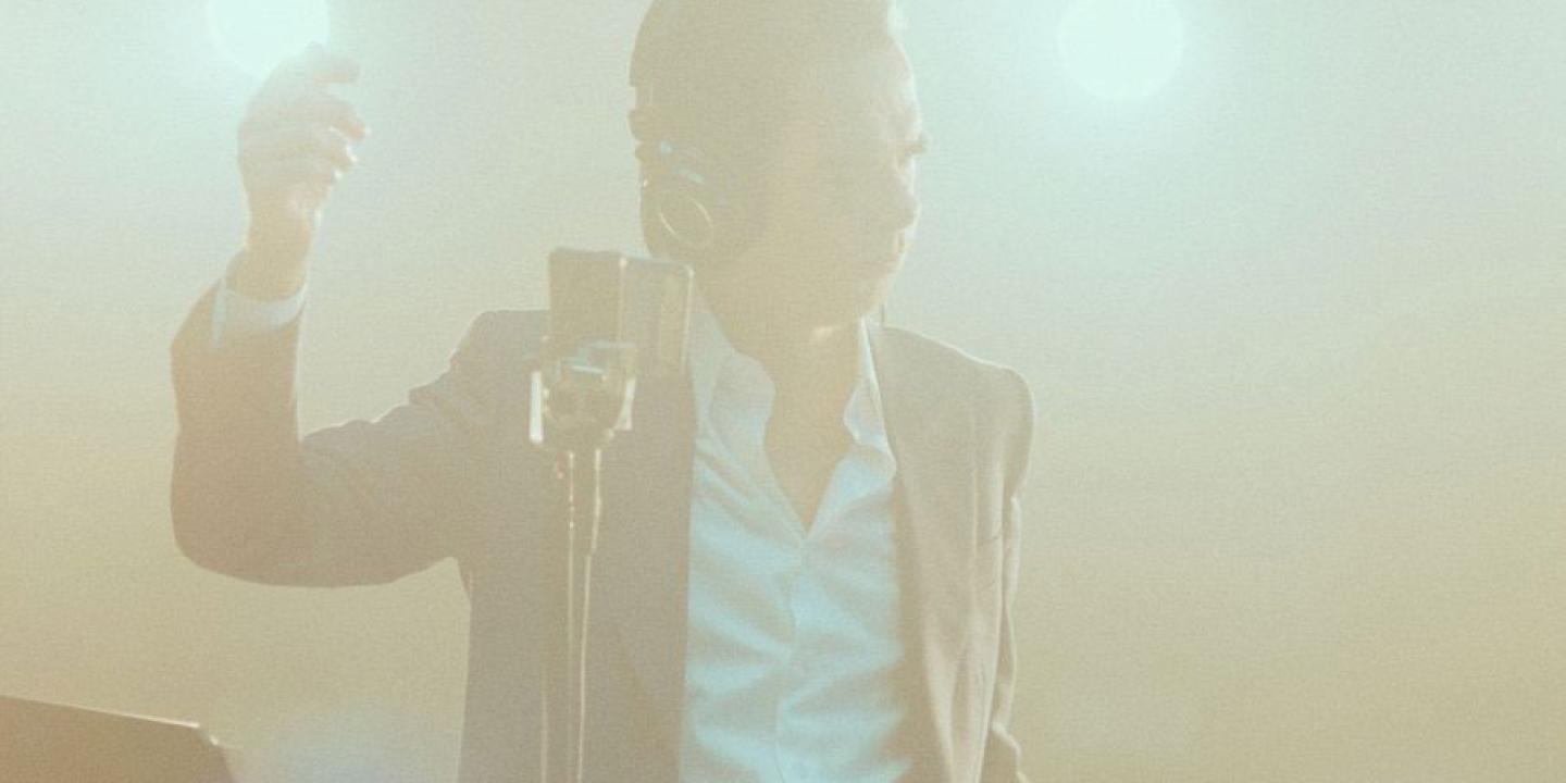 Through illuminated dry smoke, a figure stands tall, holding a light up to his head.