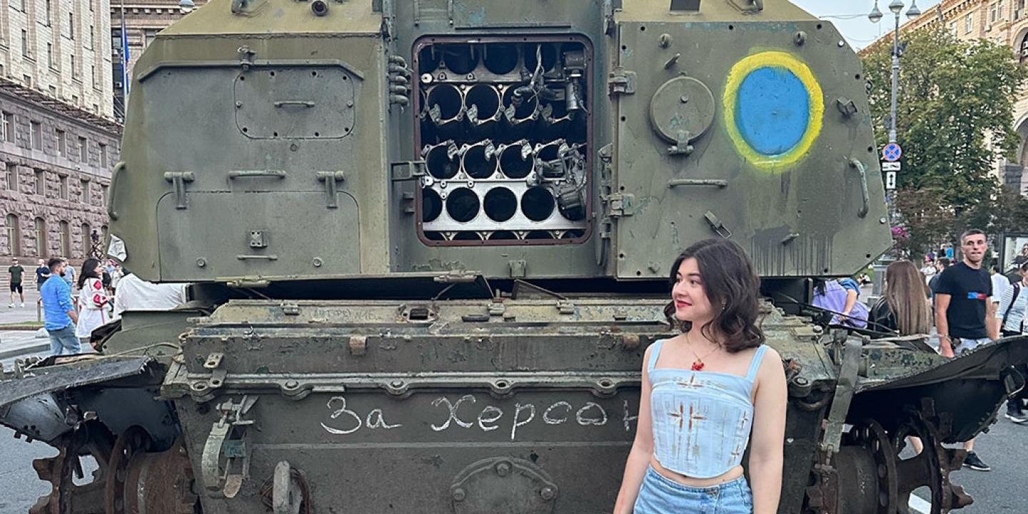 A woman stands at the back of an armoured military vehicle, the door of which is open.
