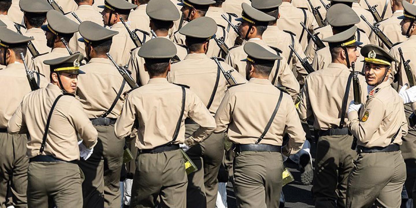 Rows of soldiers march away from the camera, two in the back row turn their heads back.