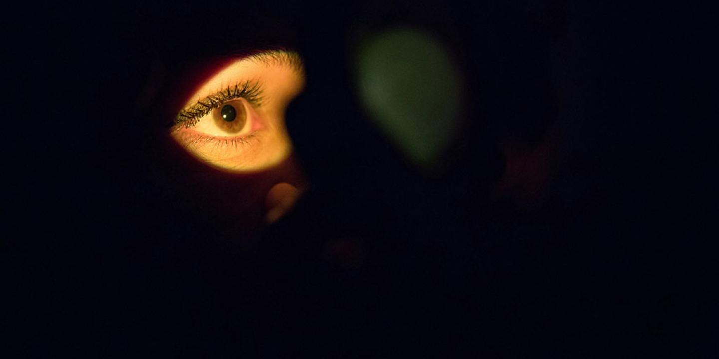 From a darkly shadowed face, a single illuminated eye stares.