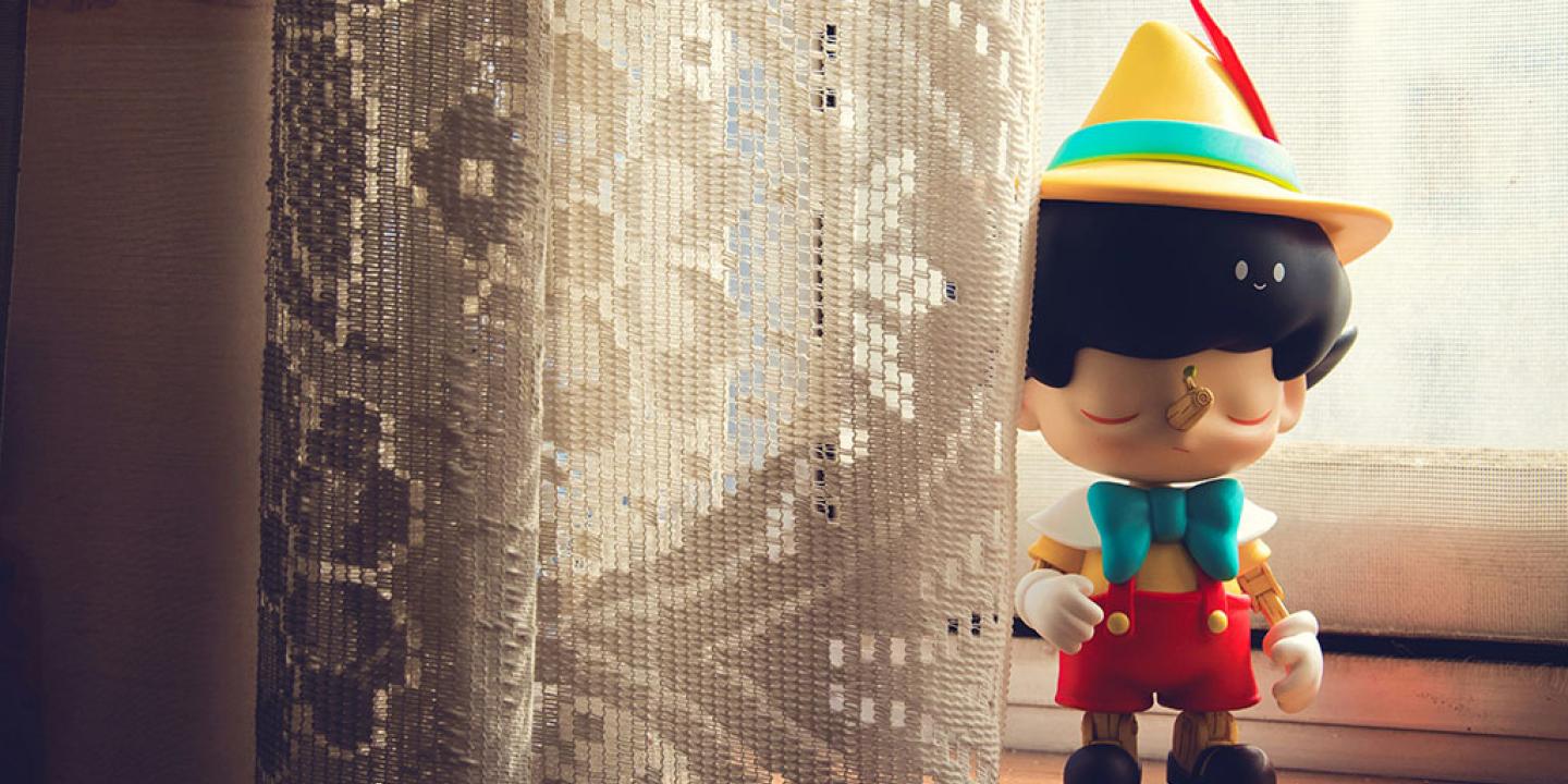 A Pinnochio figure stands on a window sill beside some net curtains.